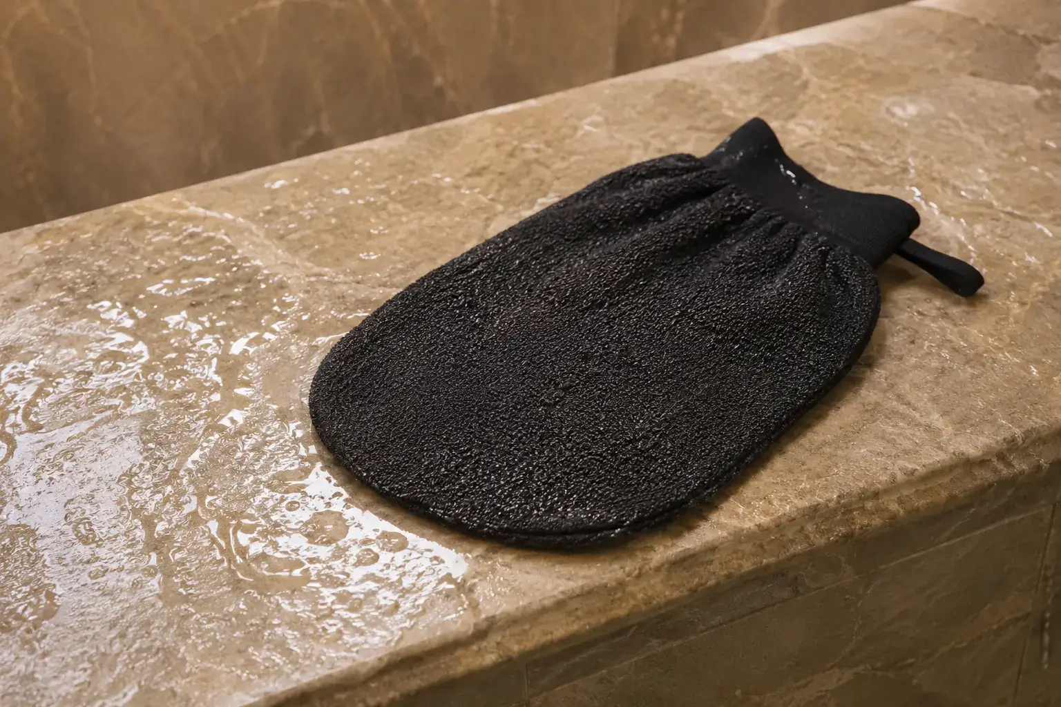 A textured exfoliating glove next to a bowl of body scrub, s